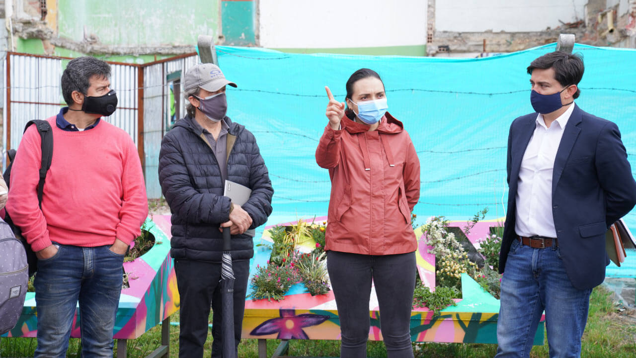 Mujer explicando y tres hombres prestando atención junto a ella, todos con tapabocas